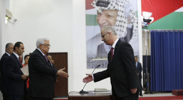 Palestinian Prime Minister Rami Hamdallah (r) shakes hands with Palestinian President Mahmoud Abbas during a swearing-in ceremony of the unity government, in the West Bank city of Ramallah June 2, 2014. Abbas swore in a unity government on Monday after overcoming a last-minute dispute with the Hamas Islamist group.