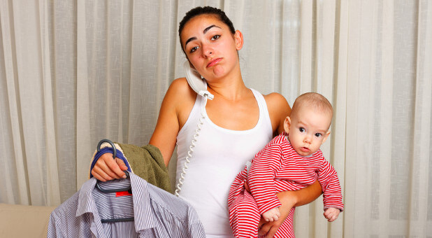young mom holding baby and ironing clothes